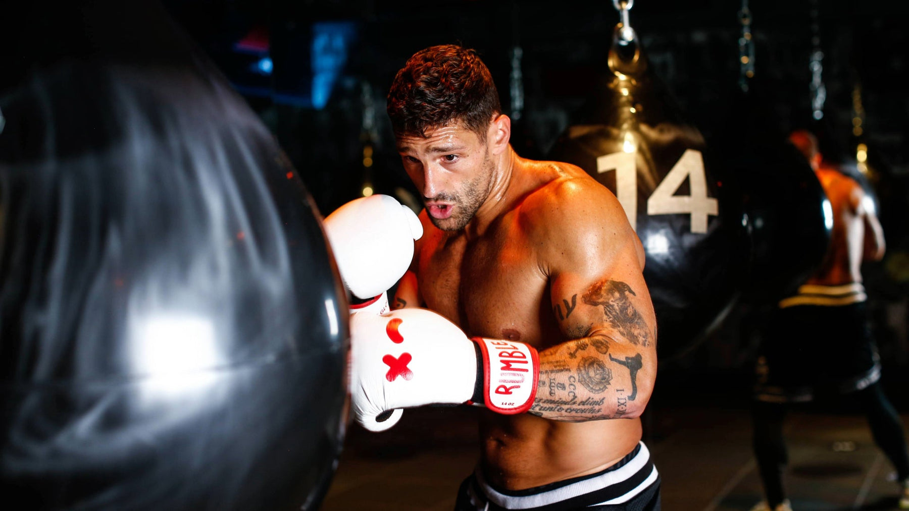 A boxer training with an Aqua water-filled punchbag in a dark boxing studio.