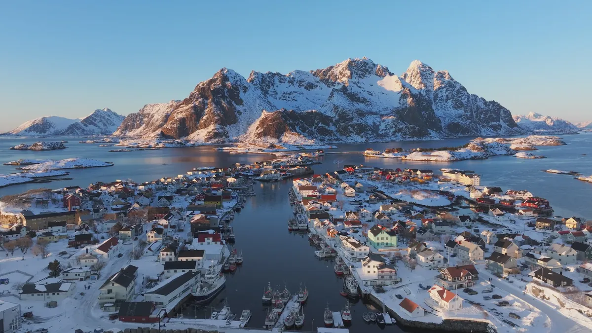 A snow-covered coastal village and mountain range seen in aerial footage from a DCX camera drone.