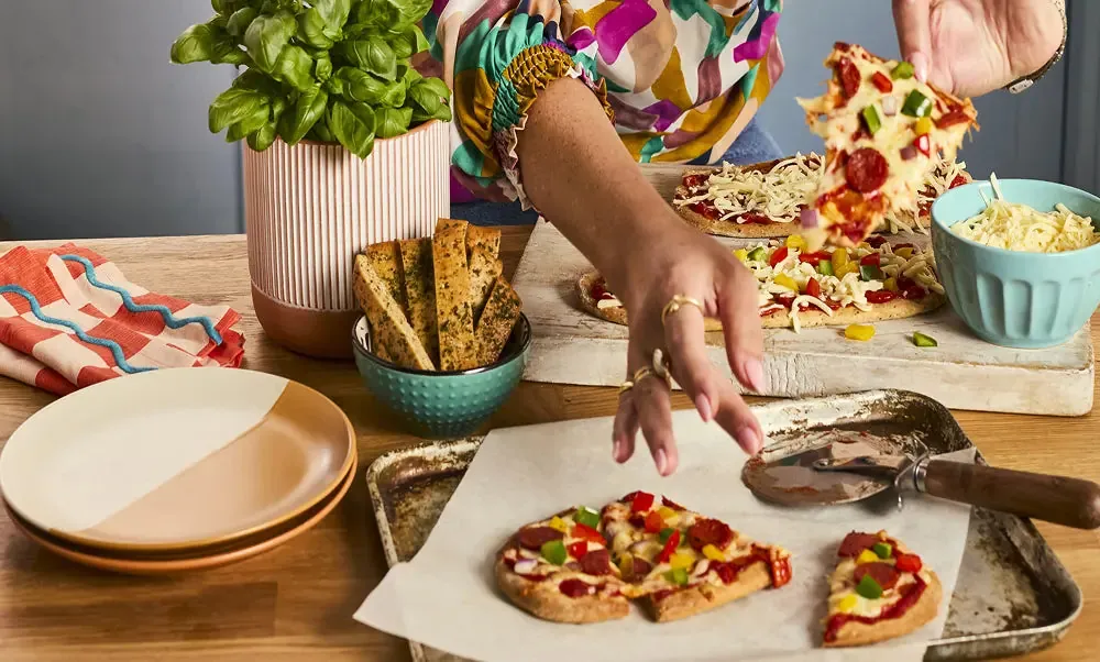 A person serving small low-carb pizzas and flatbreads at a colourful kitchen table for Heylo.