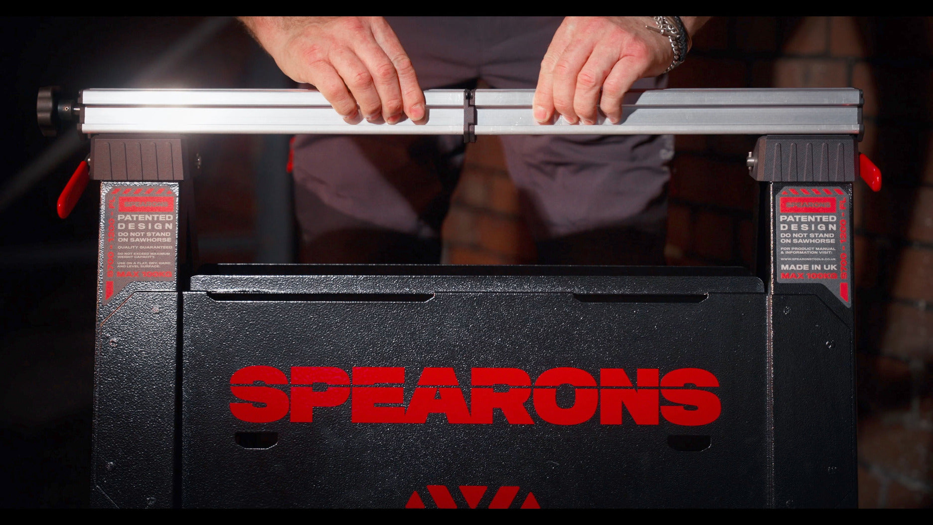 Hands adjusting the silver top rail of a black and red Spearons saw horse.